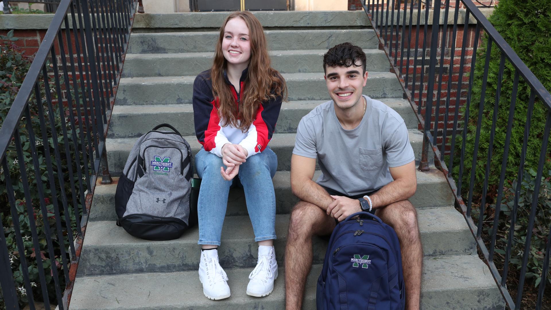 male and female Ƶapp sit on outdoor stairs with backpacks