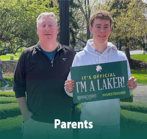 A dad posing with his son who has decided to attend Ƶapp. The son holds a poster reading "It's Official. I'm a Laker!"